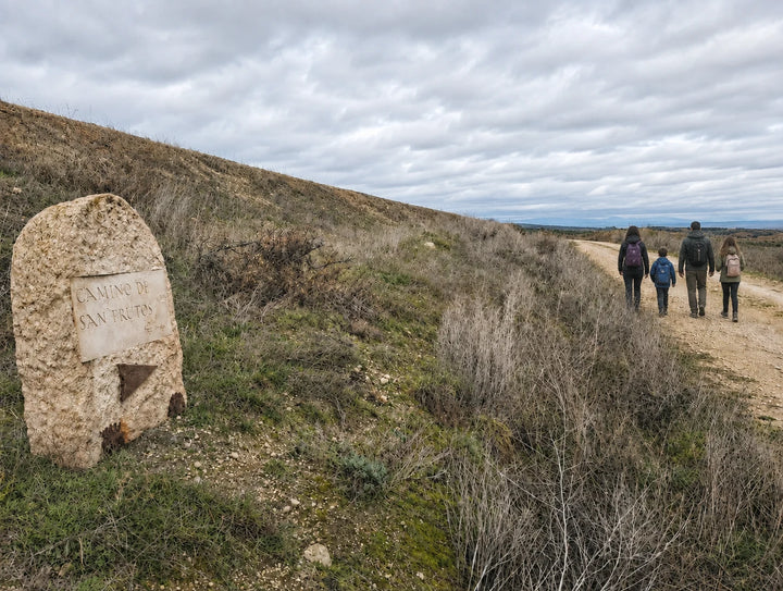 Familia con dos niños haciendo senderismo de espaldas por el Camino de San Frutos, junto a un mojón