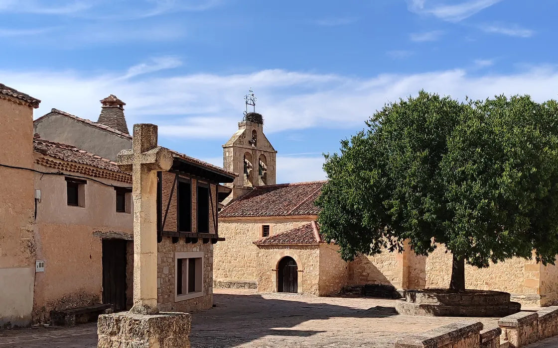 Casas de piedra, cruz, campanario y un árbol en La Matilla (Segovia).